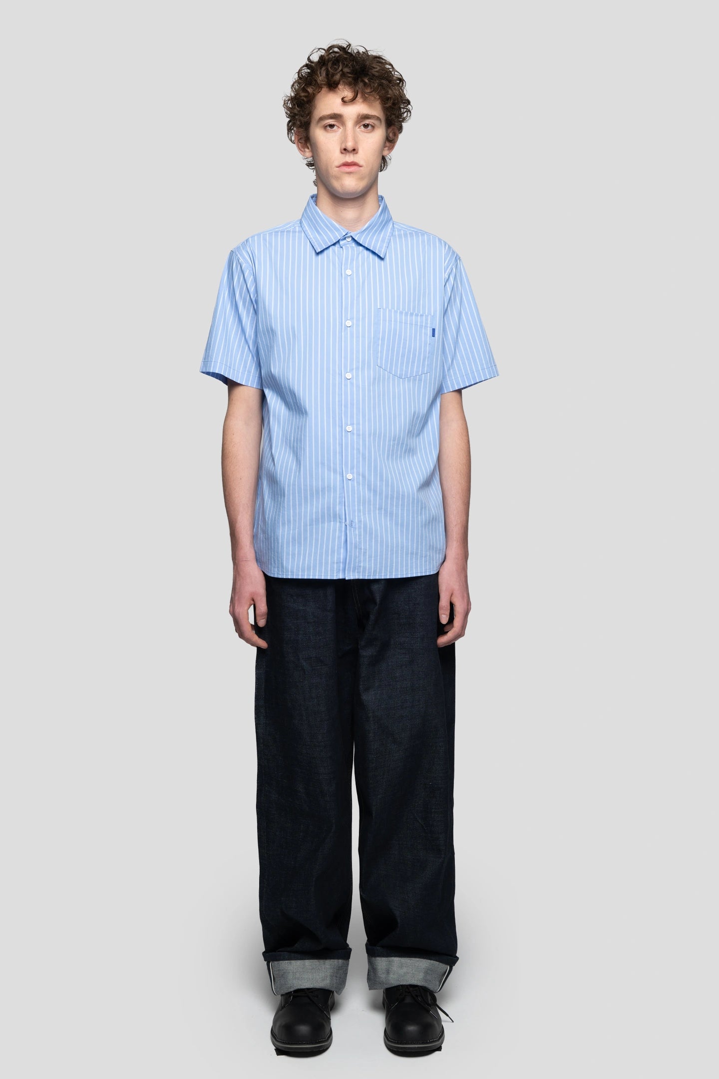 Model wearing a skater style blue stripped shortsleeve shirt with cuffed denim