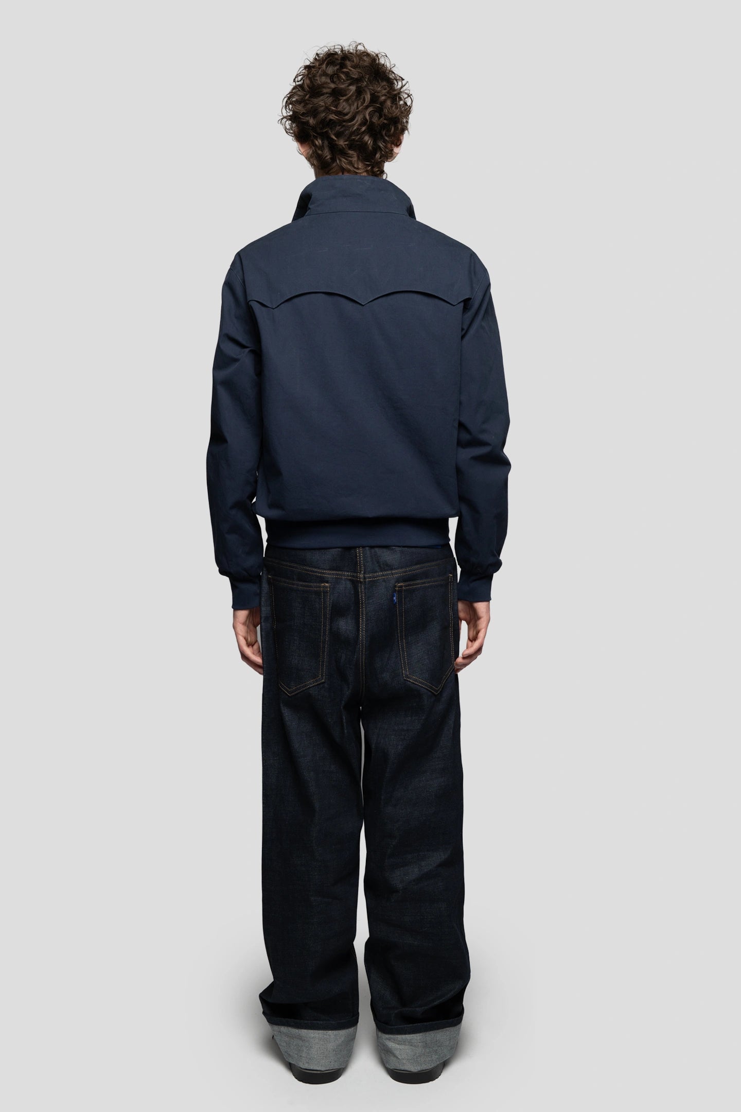 Model posing back showing a navy blue harrington jacket and heavy cotton denim