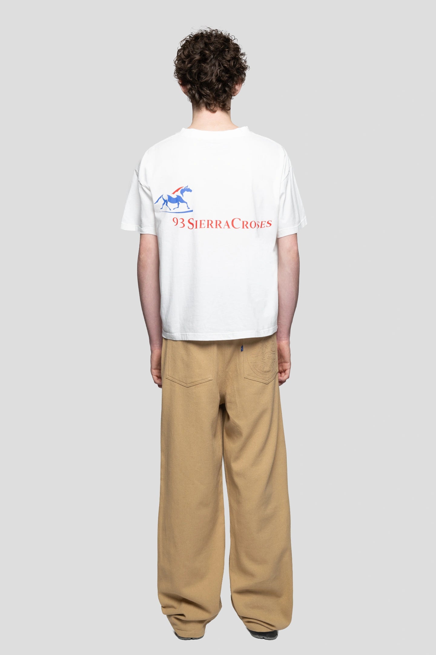 Model wearing a white t-shirt with horse logo graphic and beige working pants