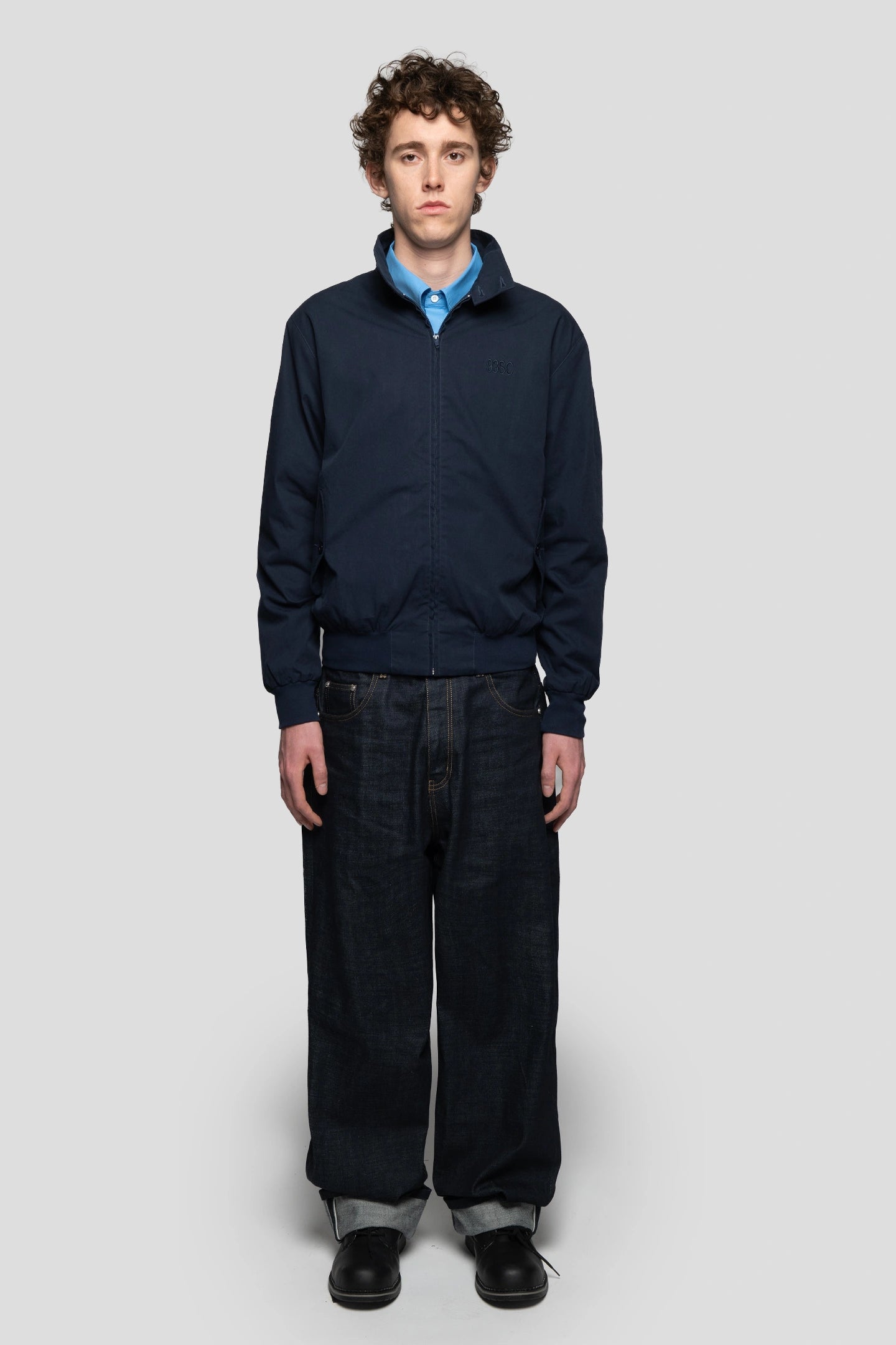 Model wearing a zip-up harrington jacket in navy blue color with baggy denim nd black boots