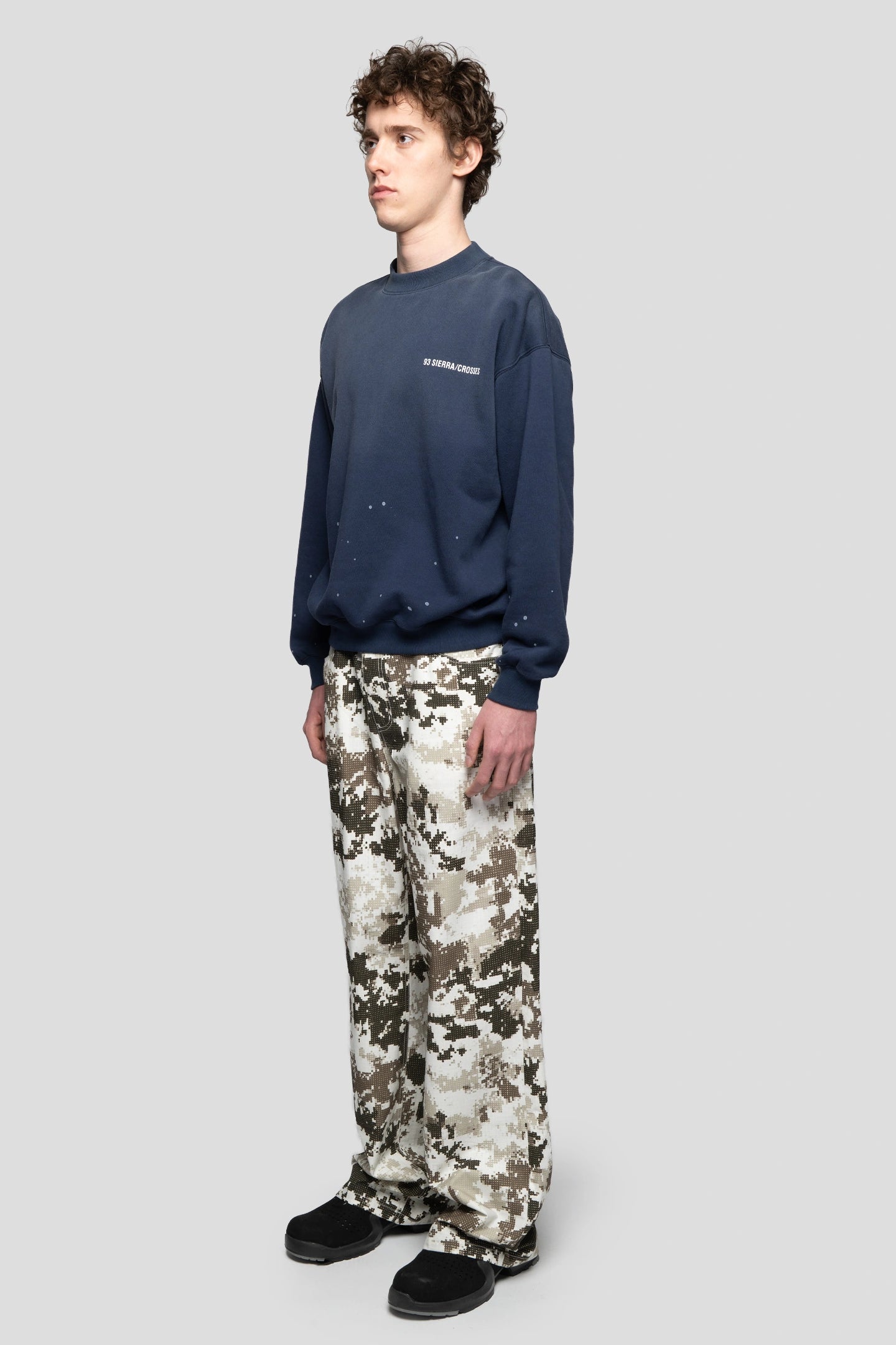 Model wearing a navy crewneck with splatter paint and negative camo pants