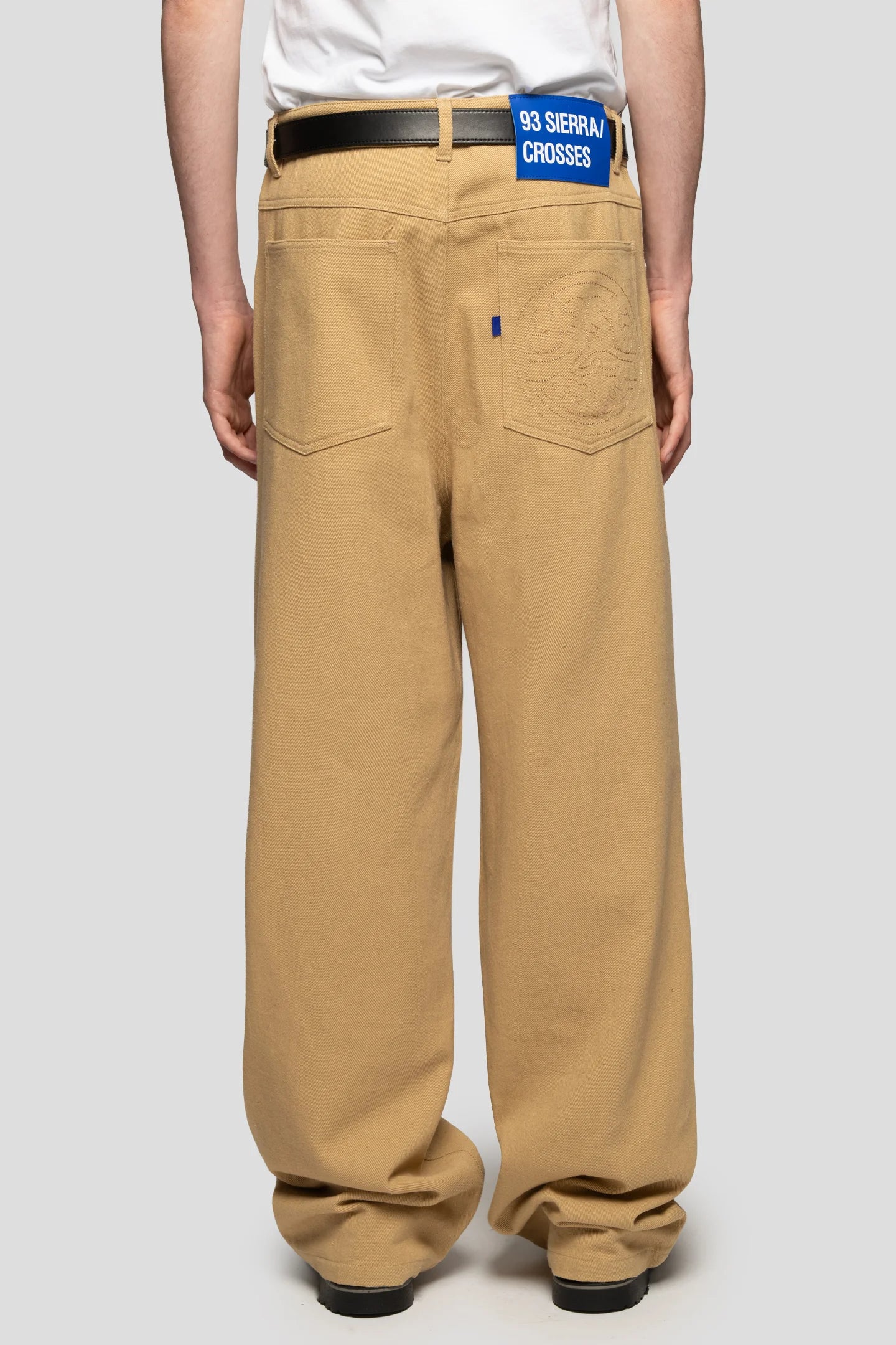 Back view of model wearing yellow camel color wide leg jeans with branded leather patch label 93 sierra crosses