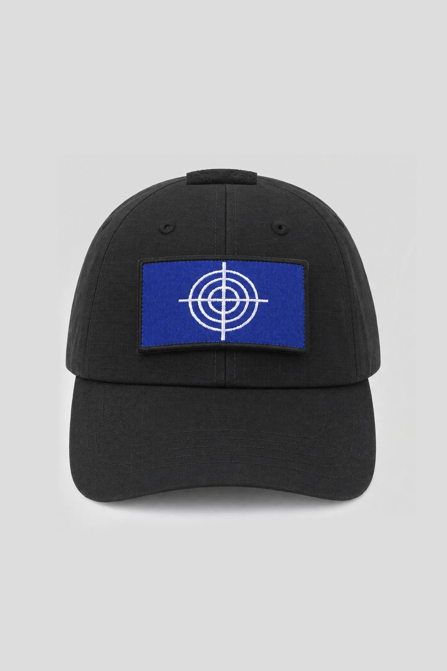 Model wearing the Crosshair Black Hat, a black ripstop cap with blue crosshair patch by 93 SIERRA/CROSSES