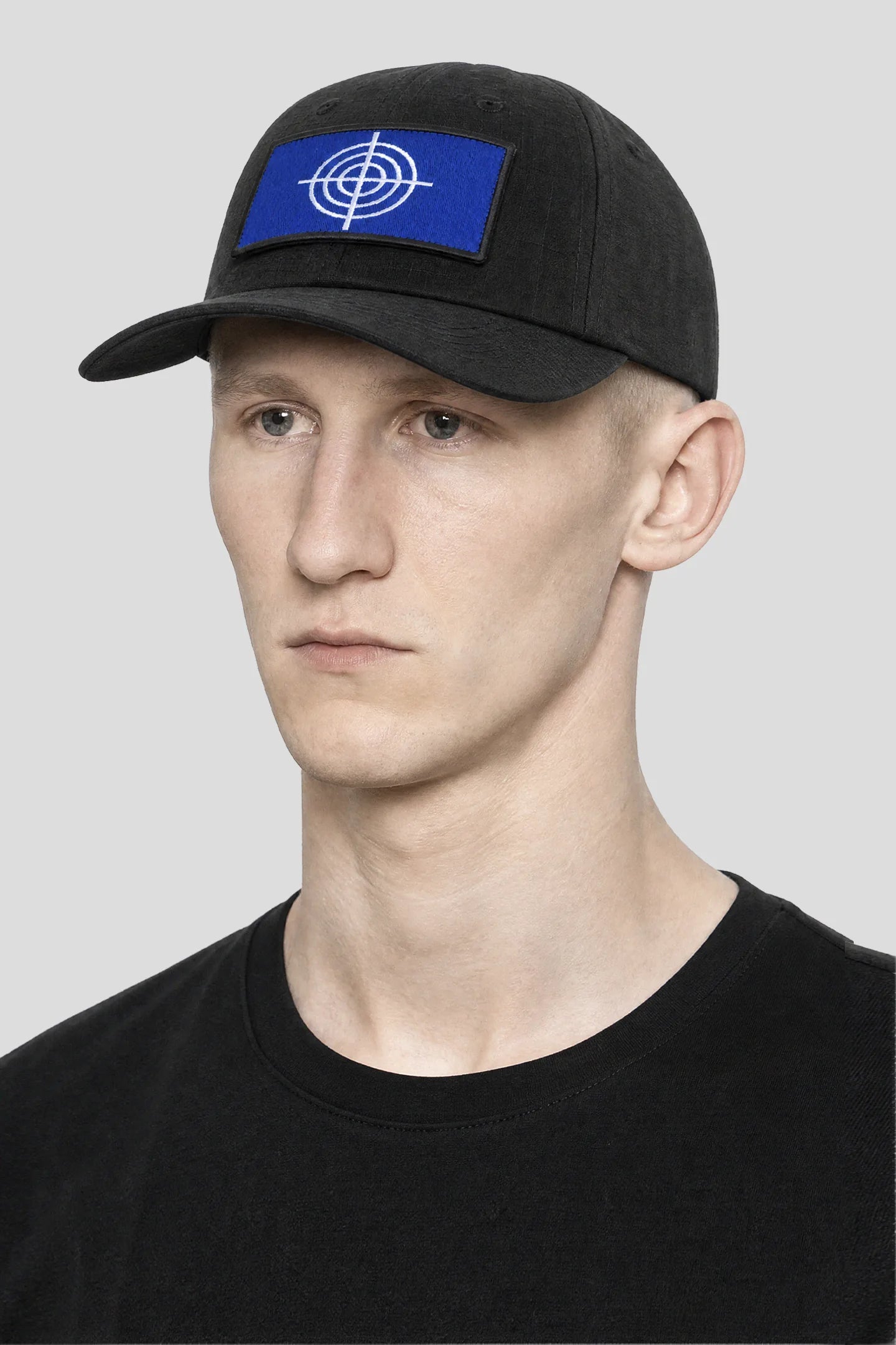 Model wearing the Crosshair Black Hat, a black ripstop cap with blue crosshair patch by 93 SIERRA/CROSSES