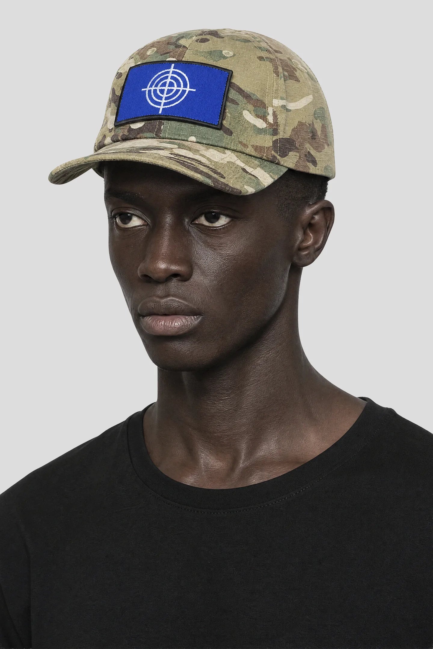 Model wearing the Crosshair Camo Hat, a camouflage cap with blue crosshair patch by 93 SIERRA/CROSSES