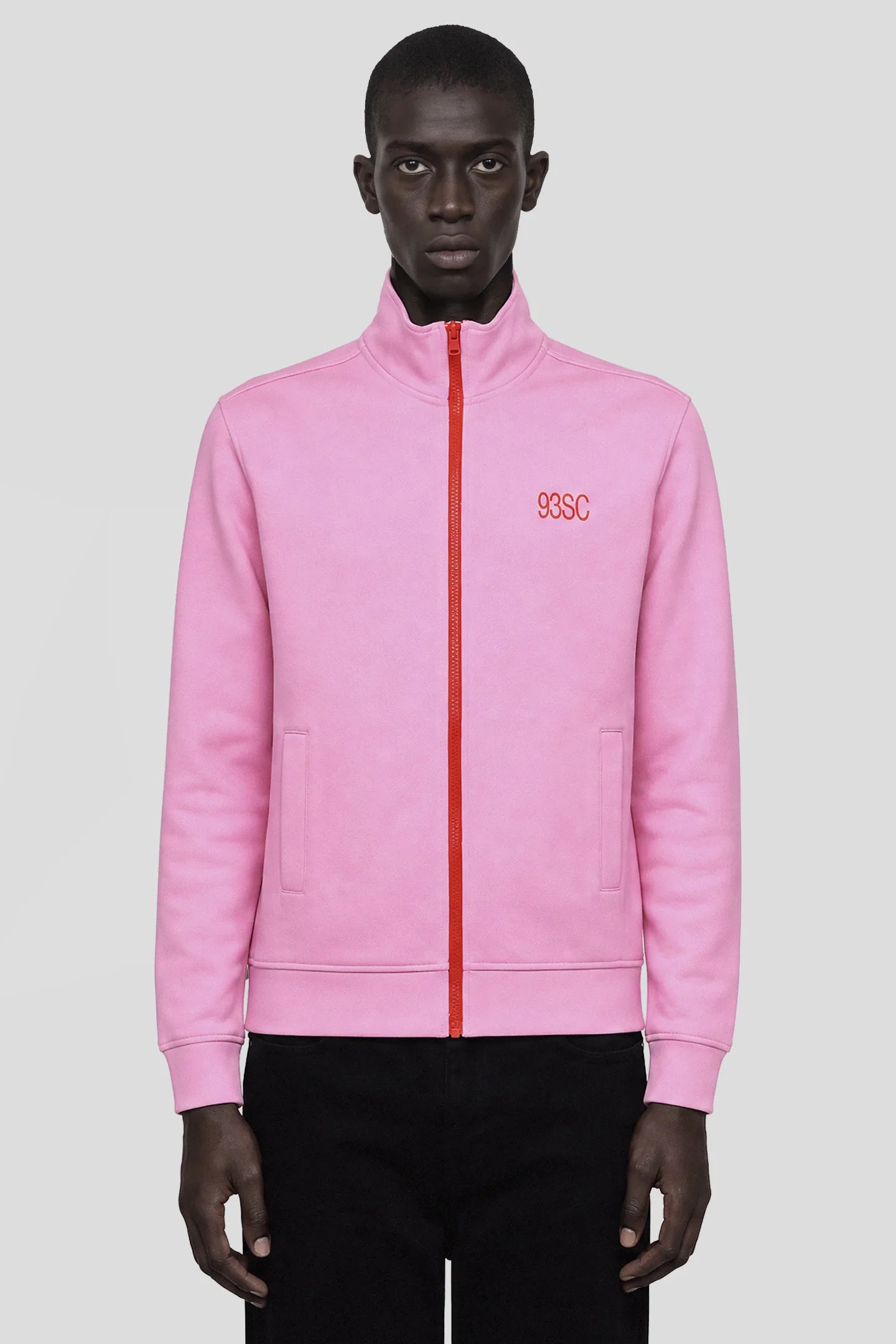 Model wearing the Pink Track Jacket with contrast red zip and 93SC embroidery, front view 93 SIERRA/CROSSES