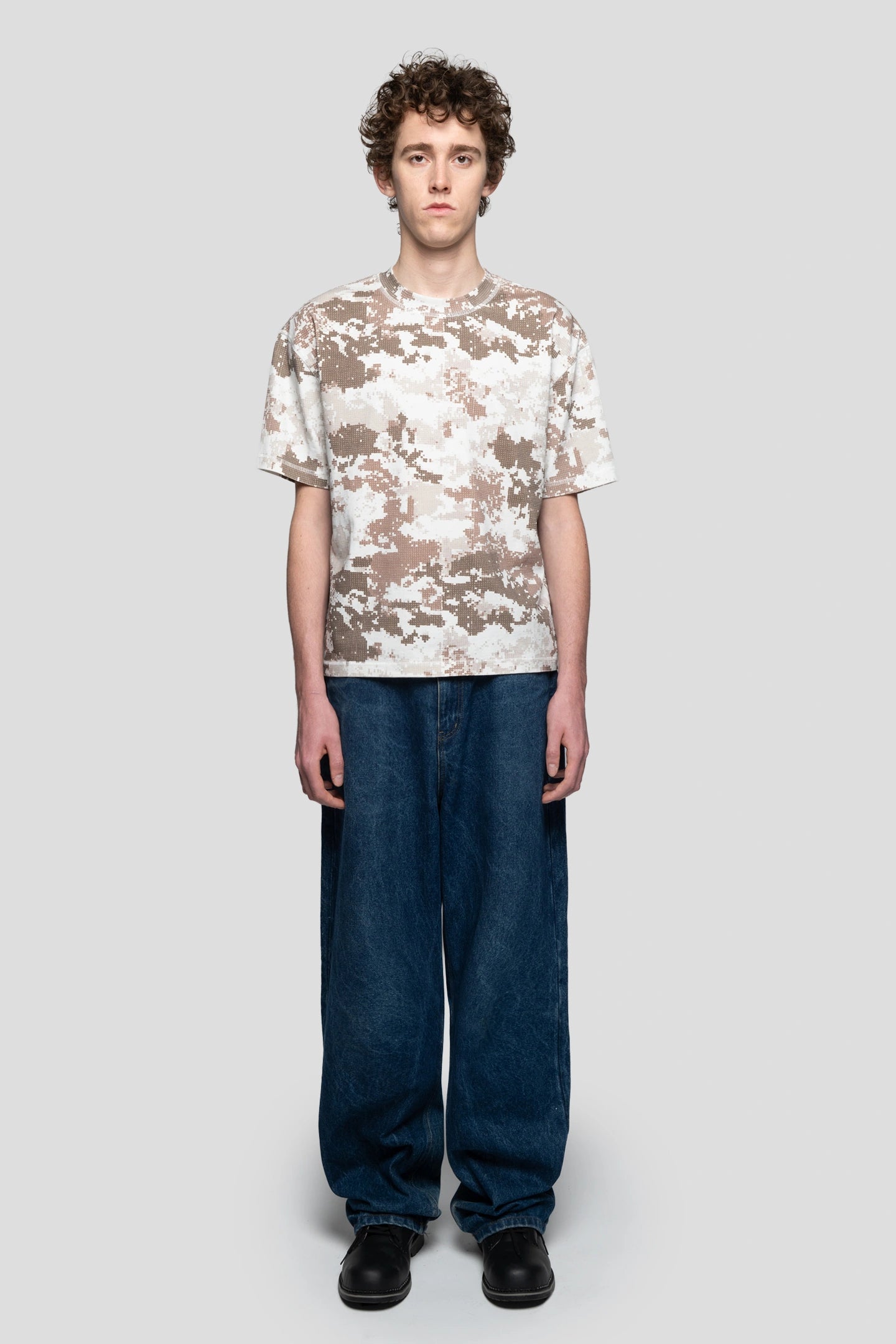 Model wearing the new digital camo brown t-shirt of the new collection of 93 sierra crosses ss26 with jeans and boots