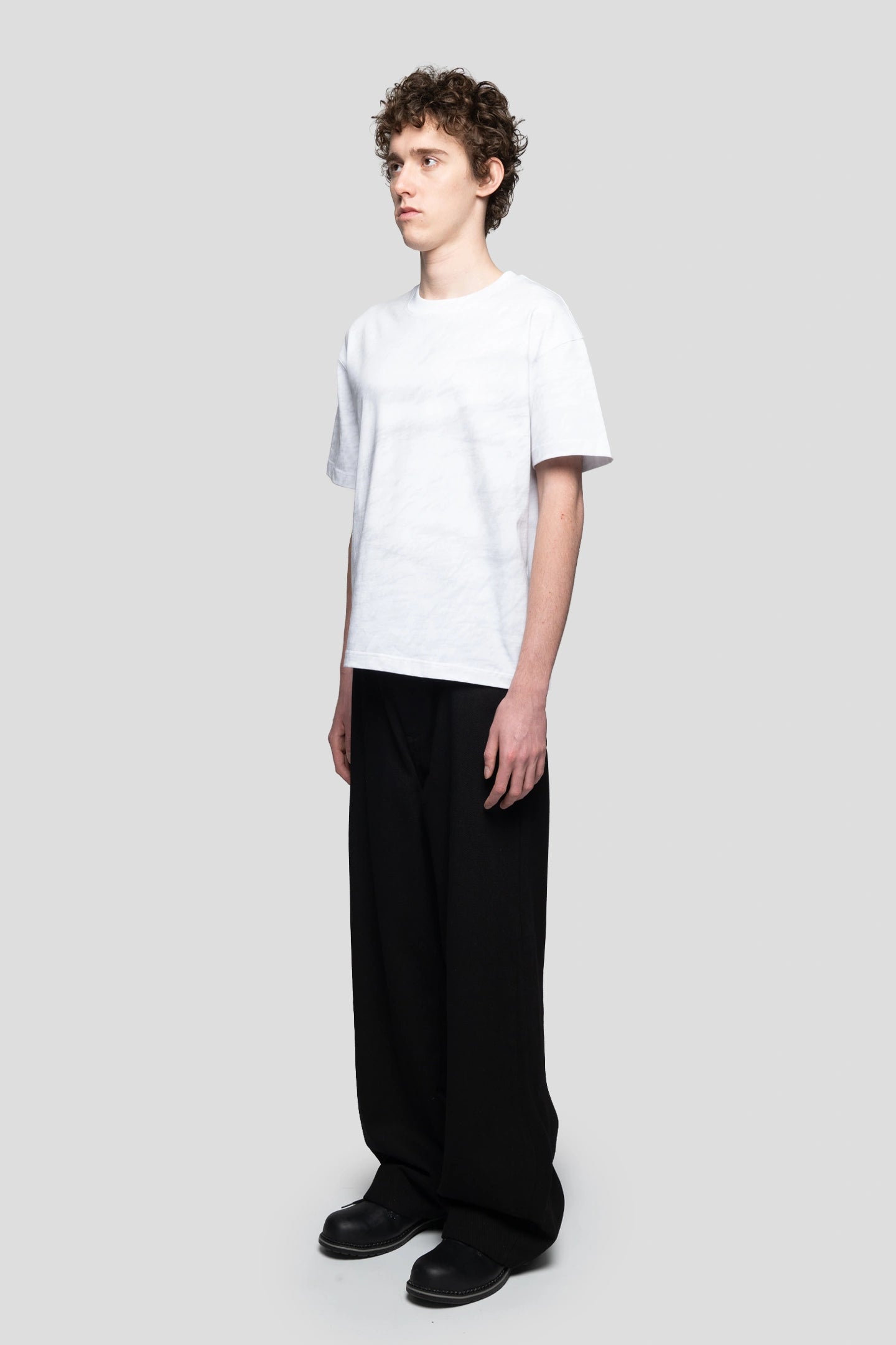 Front view model wearing wrinkled paper print tee  with relaxed black pants and boots 93 sierra crosses