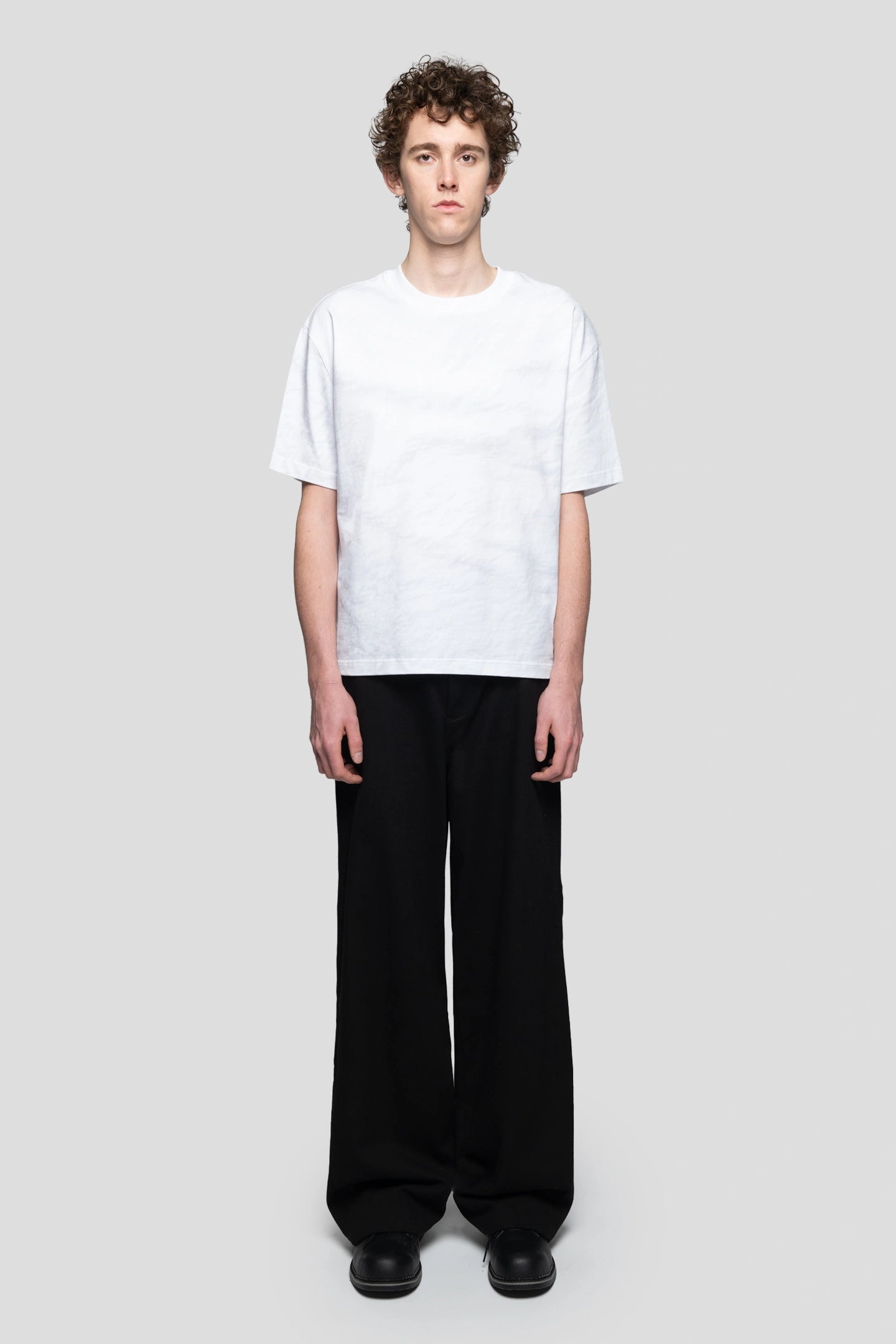 Front view model wearing wrinkled paper print tee  with relaxed black pants and boots 93 sierra crosses